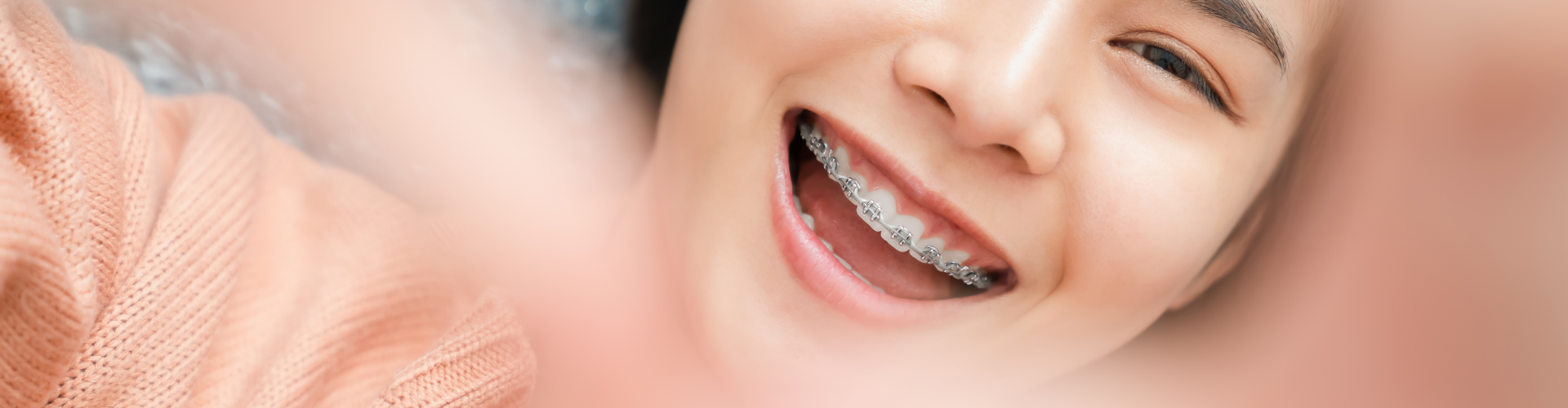 Woman's smile with metal braces seen through her hands making heart shape.
